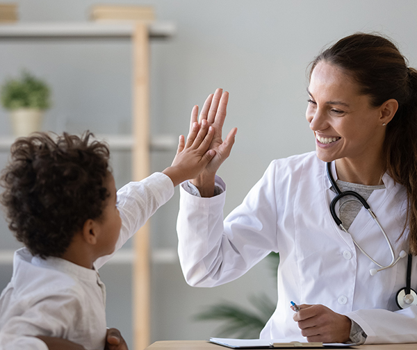 Smiling young female pediatrician give high five to little african American boy at consultation in clinic, happy woman doctor consult biracial toddler kid in hospital. Children healthcare concept