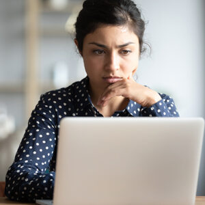 Serious frowning indian ethnicity woman sit at workplace desk looks at laptop screen read e-mail feels concerned. Bored unmotivated tired employee, problems difficulties with app understanding concept