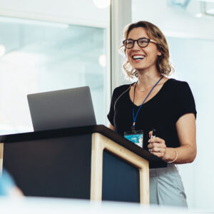 Businesswoman standing at podium with laptop giving a speech. Successful female business professional addressing a seminar.